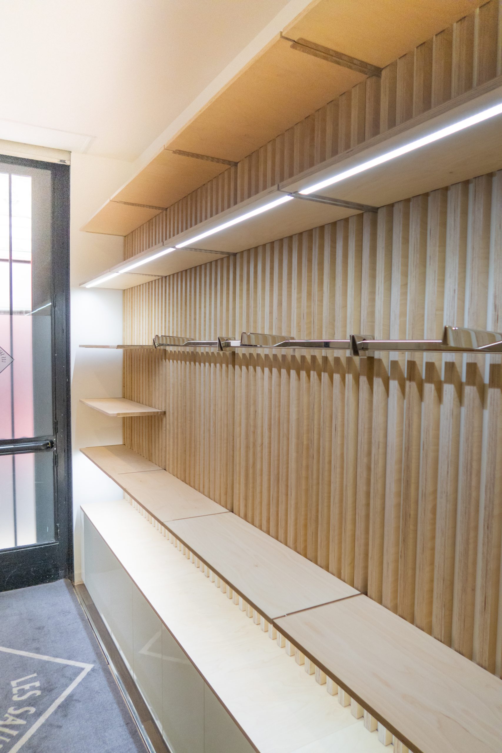 Mobilier de boutique SNCM : linéaire mural en tasseaux bois avec tablettes éclairées et meubles bas en mélaminé effet laqué blanc