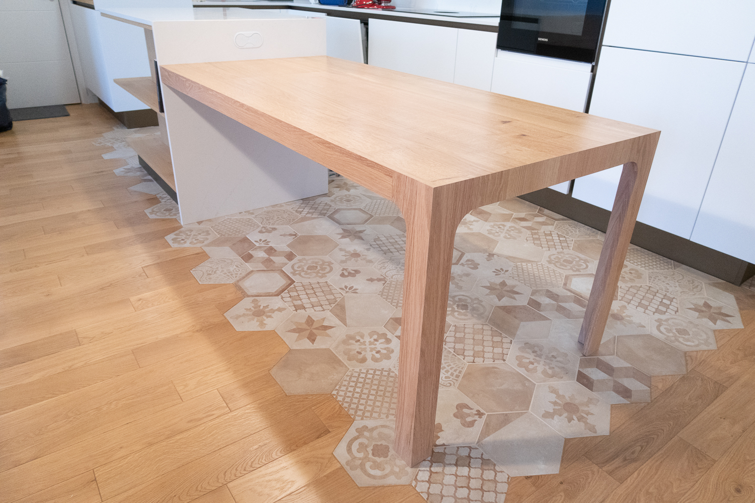 Table sur-mesure en chêne massif avec assemblage en coupe d’onglets, intégrée à un îlot de cuisine existant, finition vernie mate