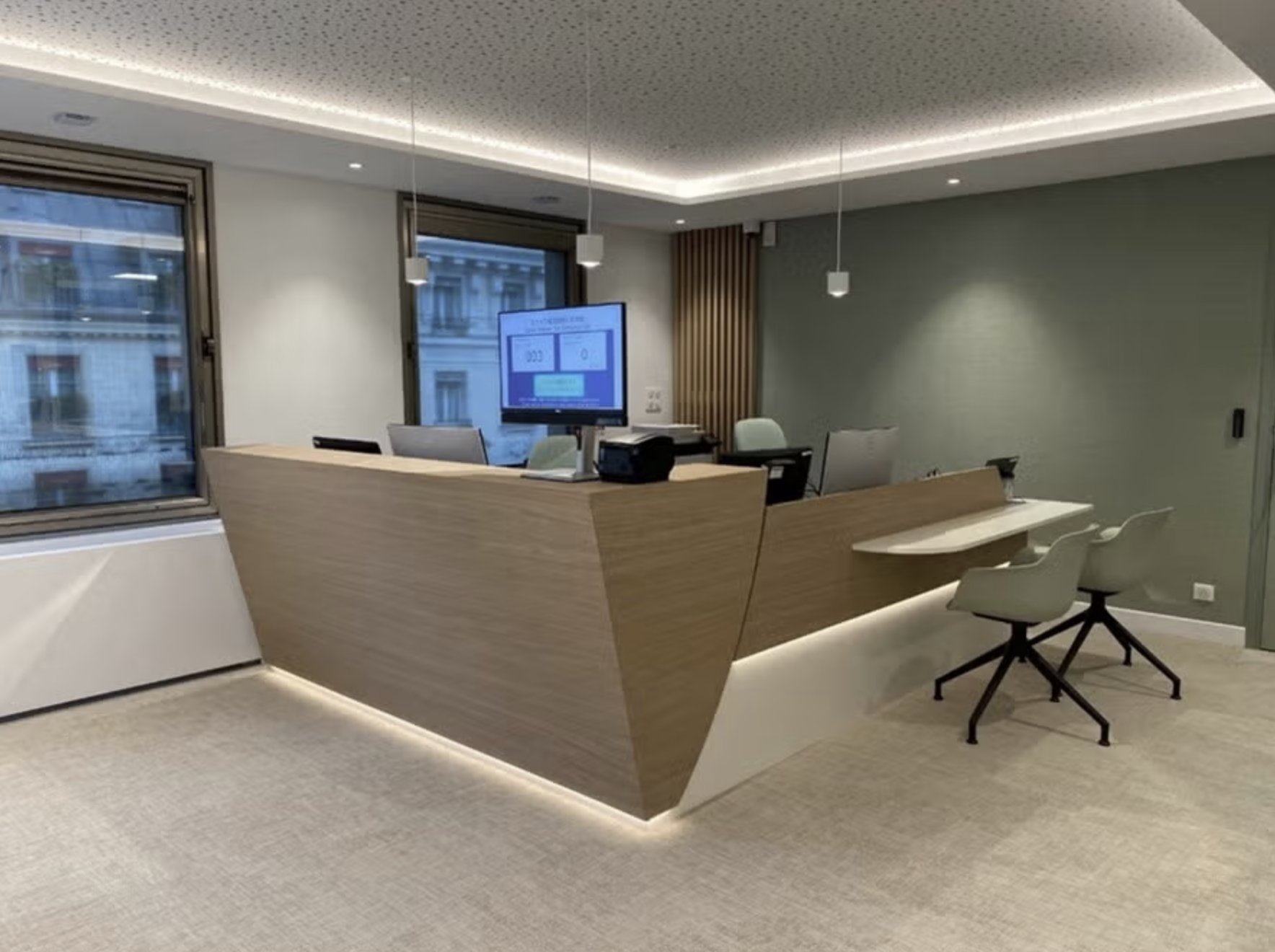 Vue du lounge d’une banque à Paris : claustra courbe en bois, banquette sur mesure, habillage mural rétroéclairé, banque d’accueil et cafétéria intégrée