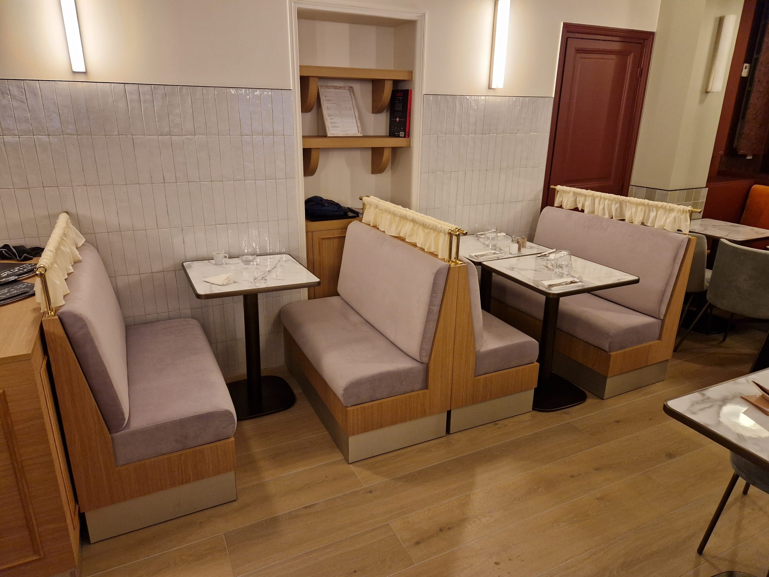 Banquettes tapissées sur mesure en bois clair avec piètement contrasté et rideau en laiton – Restaurant Gone à Paris, ambiance bouchon lyonnais