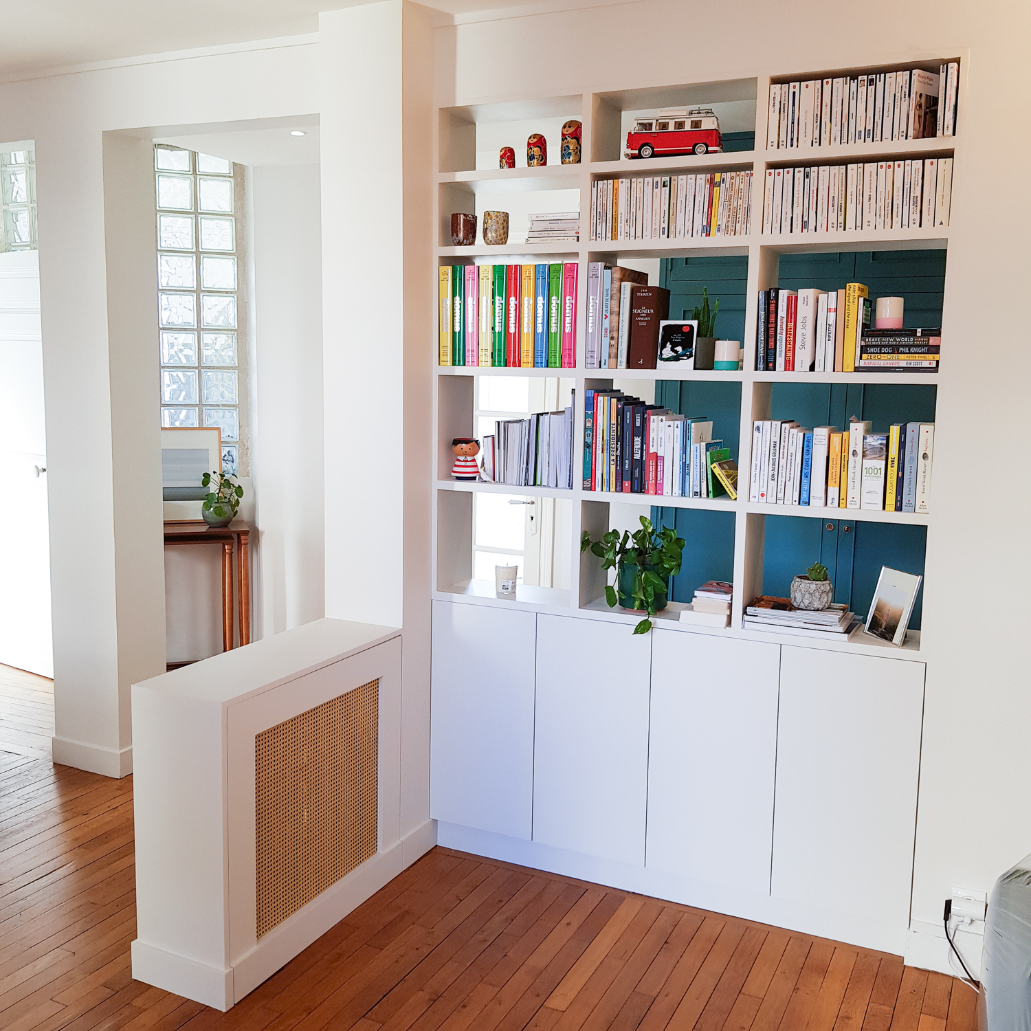 Bibliothèque sur-mesure en médium peint, cache-radiateur en cannage et coffrage de tuyauterie, réalisée dans un espace traversant en banlieue ouest de Paris