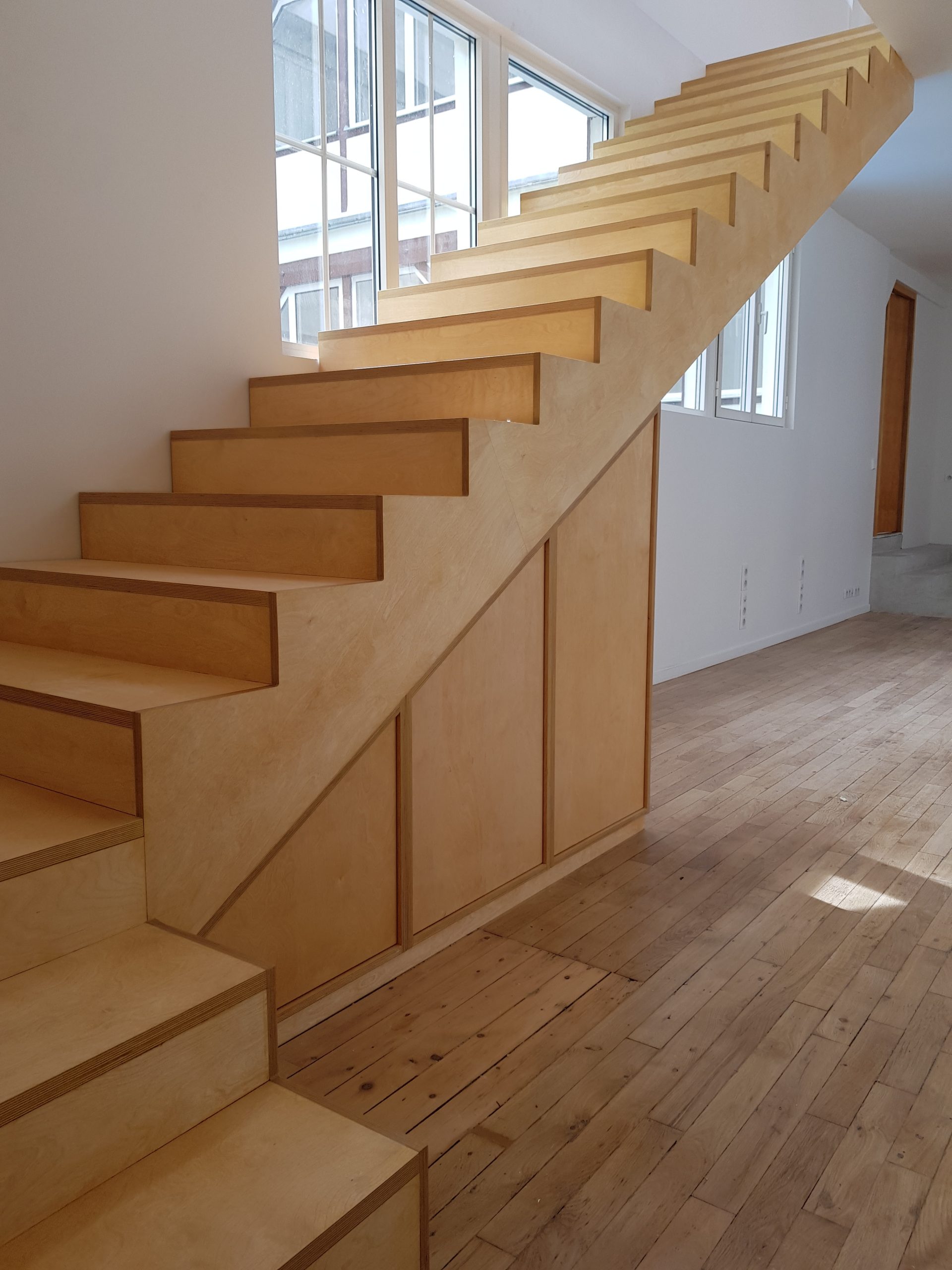 Mobilier en contreplaqué bouleau réalisé sur mesure : grand bureau cintré, bibliothèque pleine hauteur, escalier intégré et rangements dans un atelier d’artiste à Paris