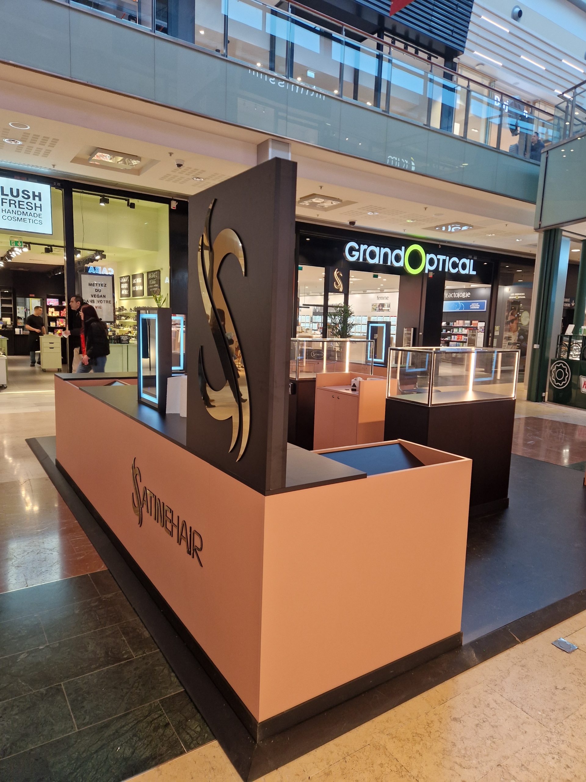 Vue d’ensemble du pop-up store Satine dans le centre commercial Vélizy 2, avec caissons en mélaminé, vitrines rétroéclairées en PMMA, meuble caisse sur mesure et enseigne totem verticale lumineuse