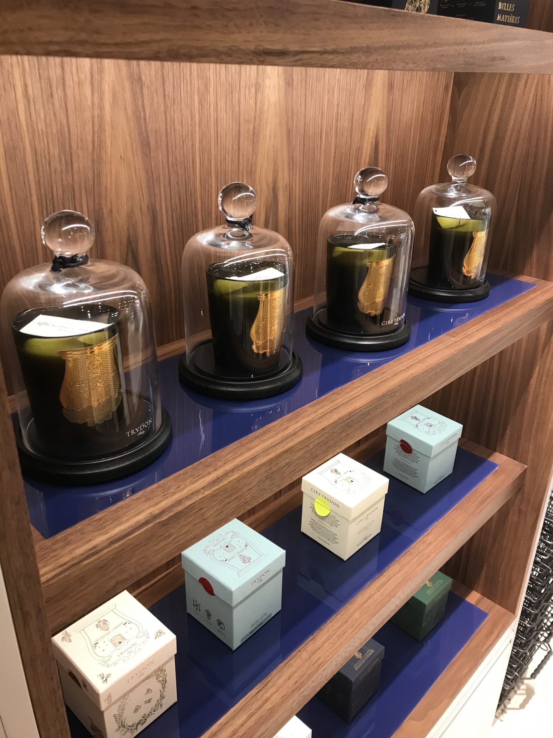 Meuble de présentation Trudon en placage noyer avec finition Rubio, tablettes en verre laqué bleu RAL client, installé aux Galeries Lafayette Strasbourg