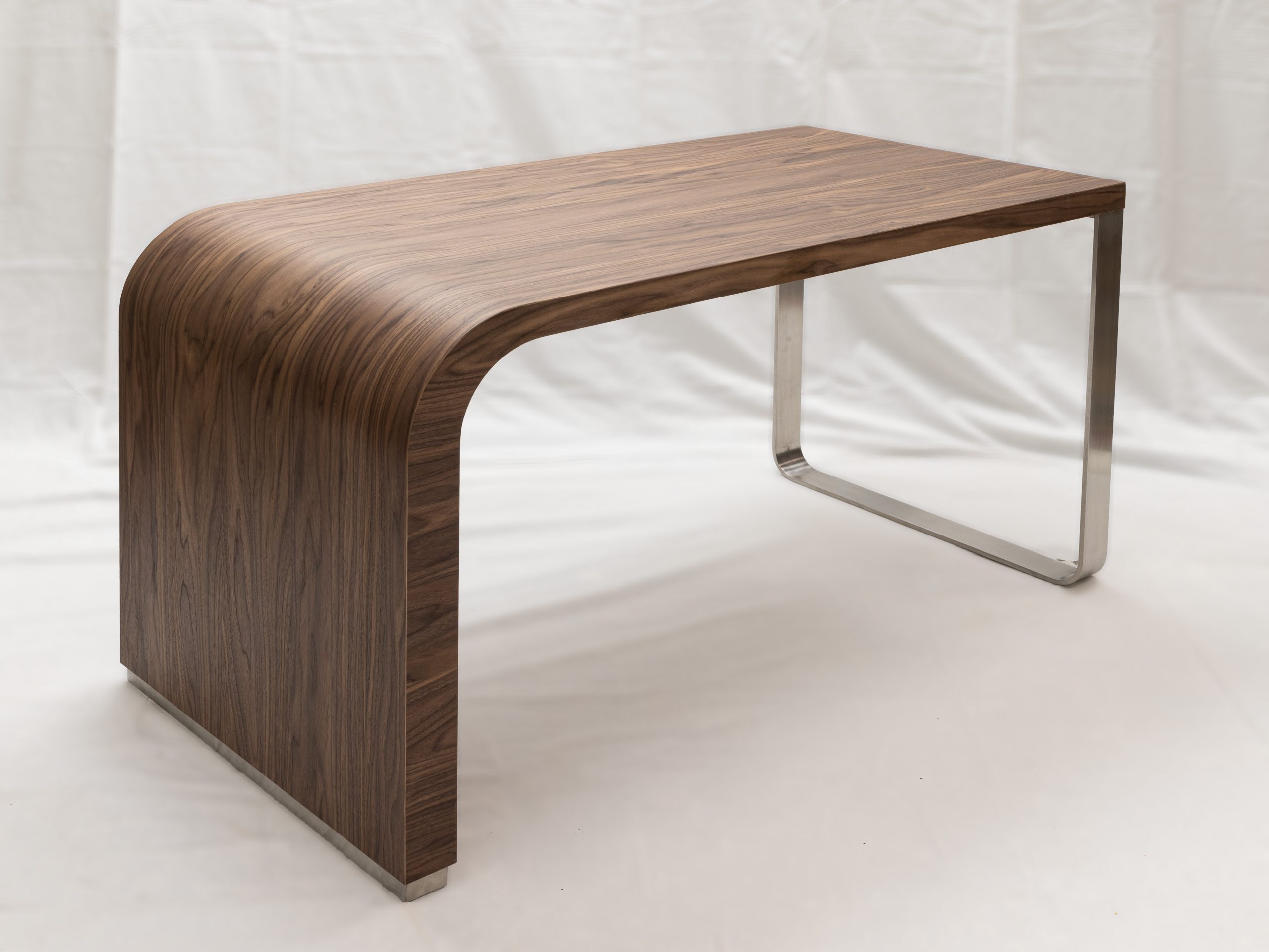 Table sur-mesure cintrée conçue pour Patricia, en placage noyer Hubler avec piétement en inox brossé, réalisée en atelier, placage fini